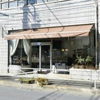 カフェ風の店舗外観、ベージュの日よけと白いフェンスが特徴的